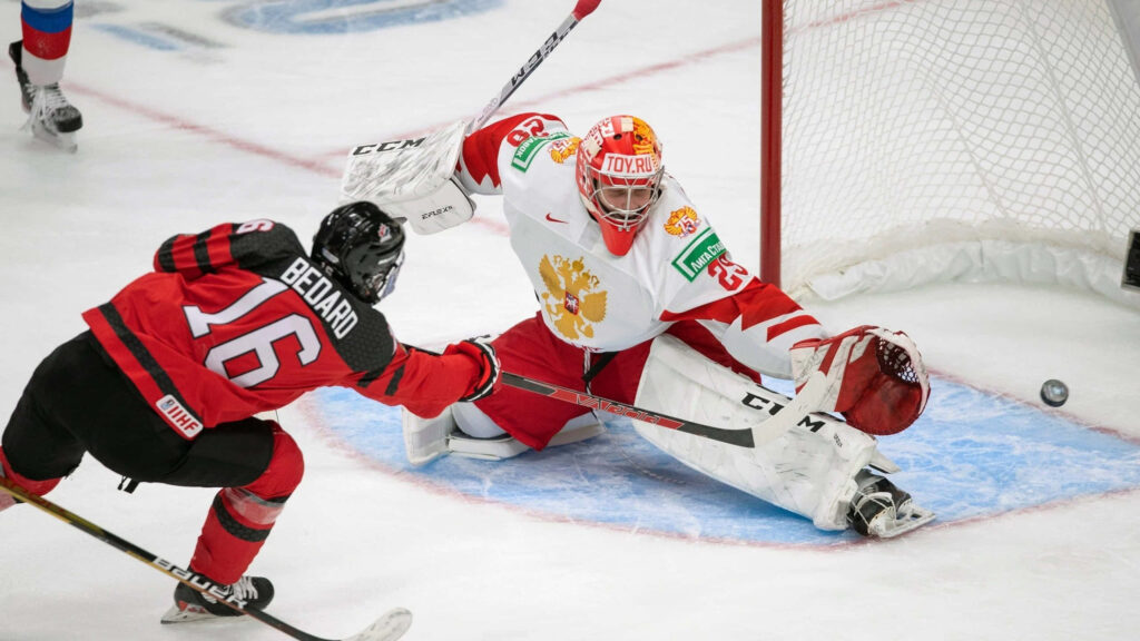 Connor Bedard shoots on goal against Russian goalie in intense hockey action with vibrant uniforms Wallpaper
