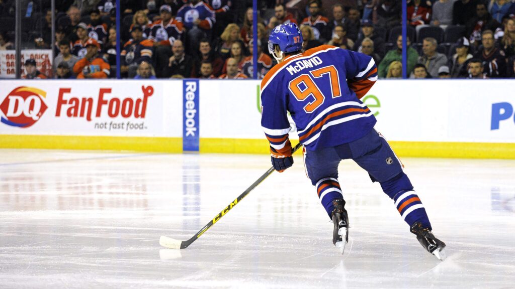 Connor McDavid Edmonton Oilers in blue orange white jersey skating during NHL game with fans Wallpaper