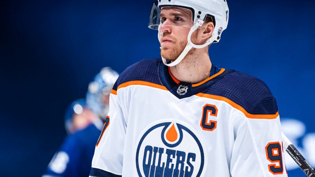 Connor McDavid Edmonton Oilers ice hockey captain in white navy orange jersey blue background Wallpaper