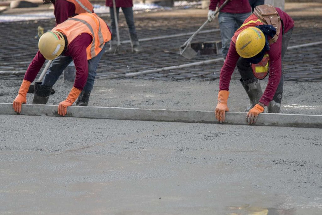 Construction workers in yellow helmets leveling fresh cement vibrant industrial concrete texture wallpaper