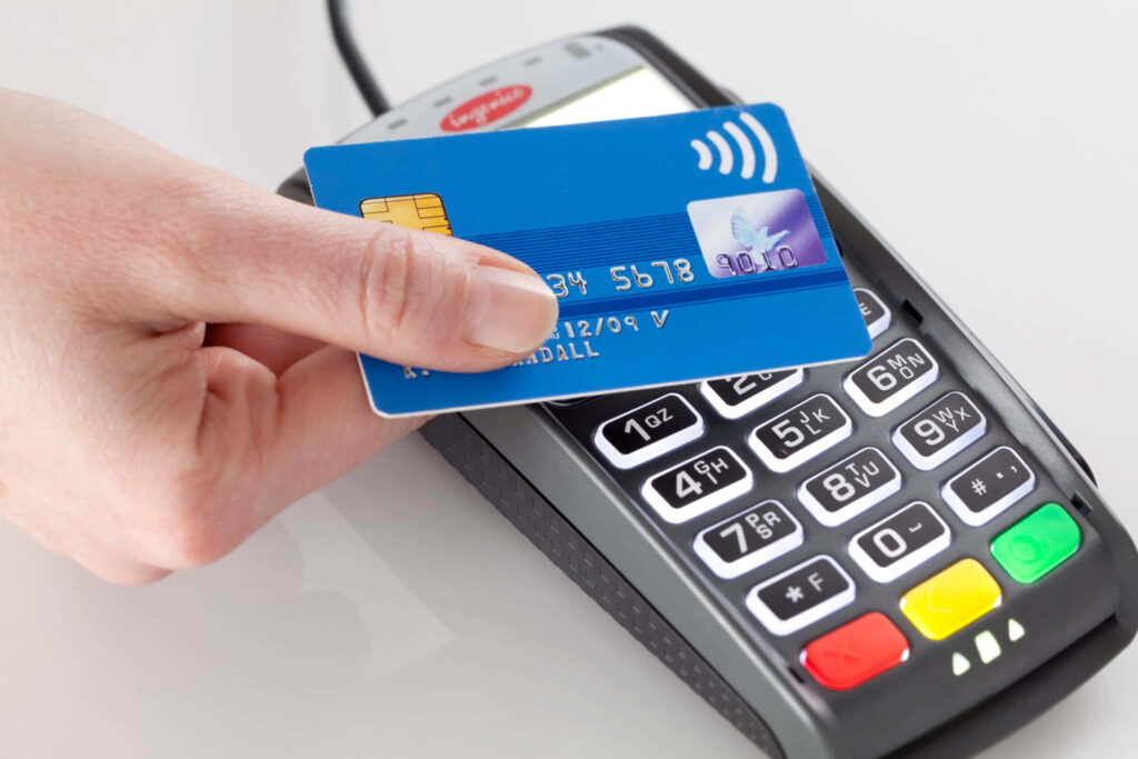 Person holding blue credit card near modern POS machine demonstrating contactless payment technology Wallpaper