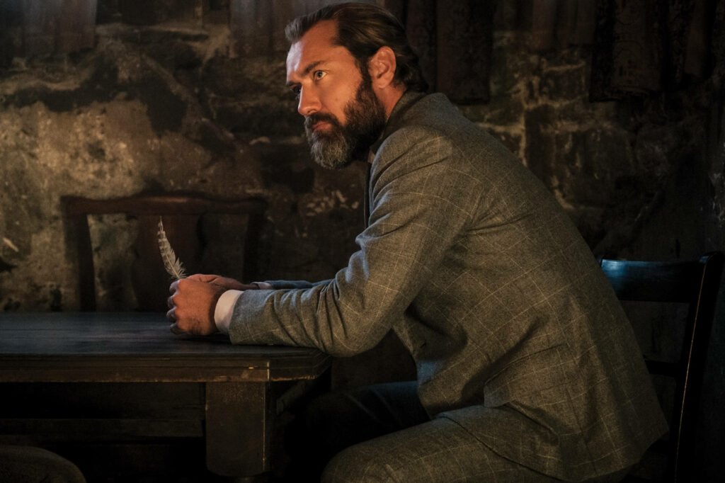 Young Albus Dumbledore in grey suit sitting contemplative in dimly lit room wallpaper background