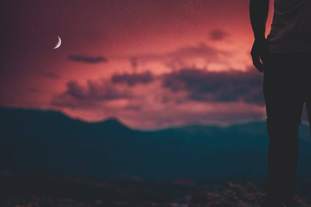 Person silhouette beneath crescent moon against striking red sky starry night wallpaper background