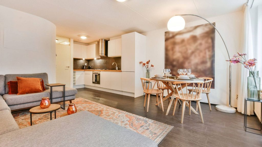 Modern open-plan apartment with kitchen wooden dining area grey sofa and patterned rug interior Wallpaper