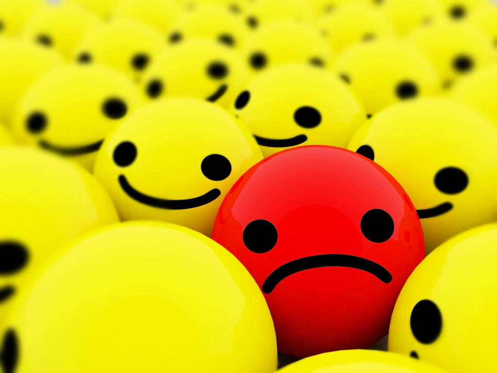 Contrasting Emotions: Lonely Red Smiley Amidst a Joyful Yellow Smileys Party Wallpaper