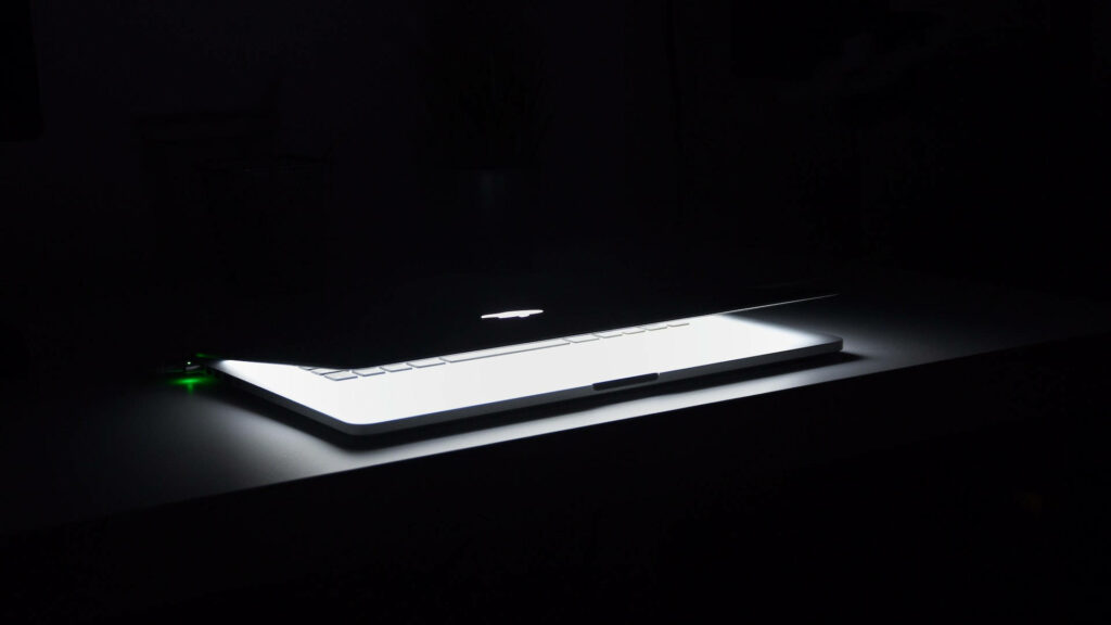 Glimpse of Illumination: A Mysterious Macbook Awakens in Darkness Wallpaper