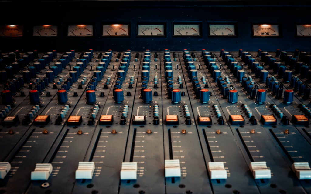 Amek audio mixing console with knobs faders and backlit VU meters in dim recording studio Wallpaper