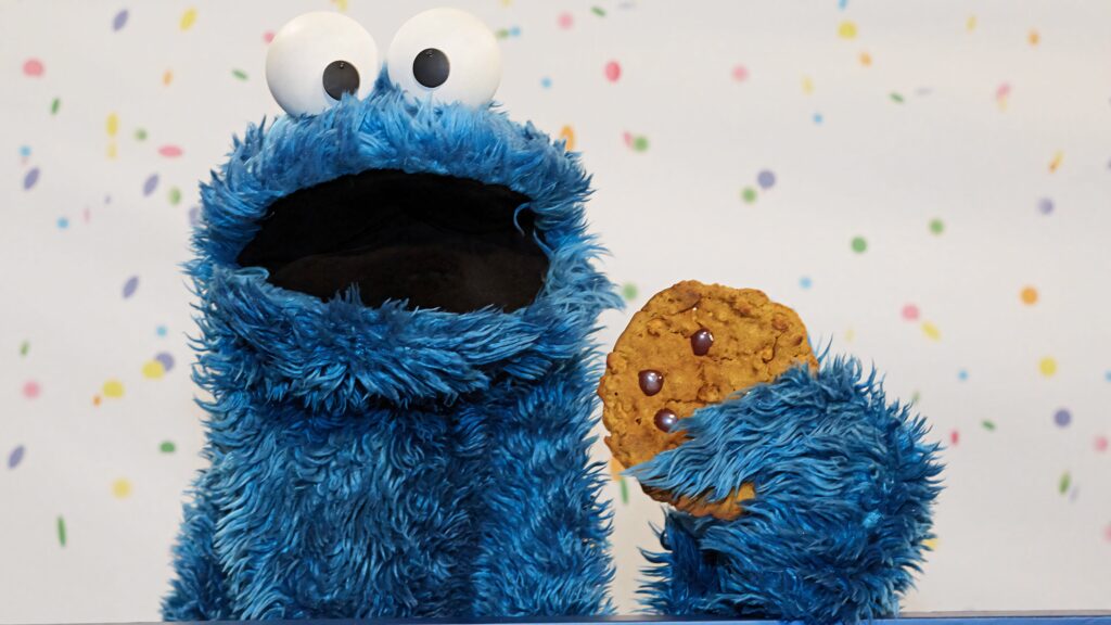 Cookie Monster holding chocolate chip cookie vibrant playful wallpaper with confetti background