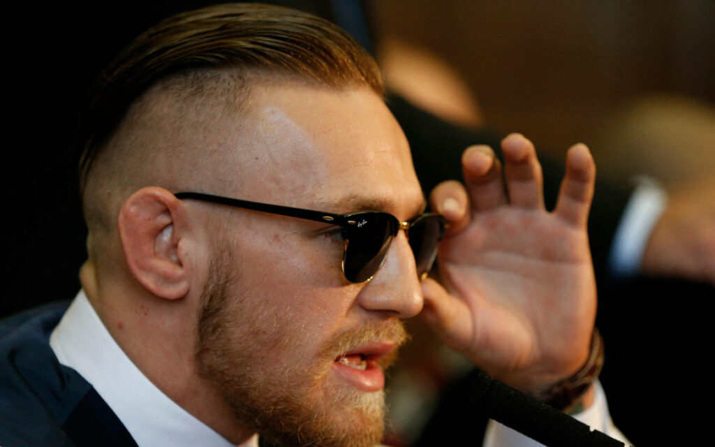 The Suave Side of Conor McGregor: A Classy Wallpaper Featuring the Irish Fighter in Sunglasses and Suit