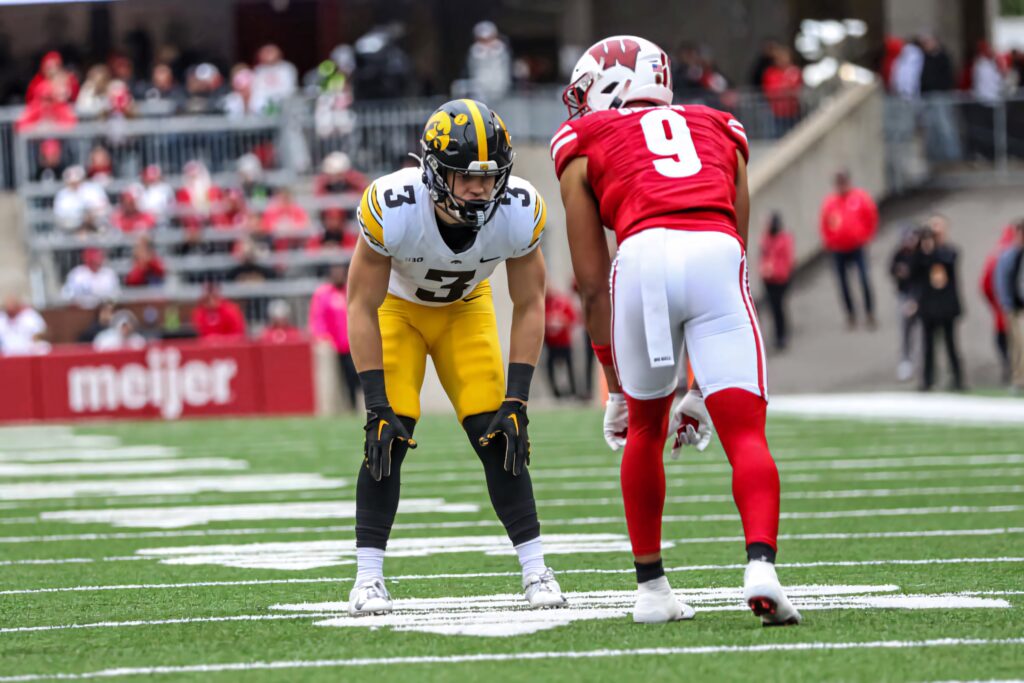 Cooper DeJean in Iowa Hawkeyes uniform defending against Wisconsin player on green turf Wallpaper