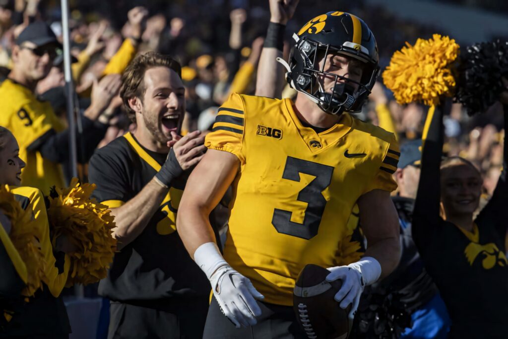 Cooper DeJean Iowa Hawkeyes football action wallpaper with fans cheerleaders black gold uniform