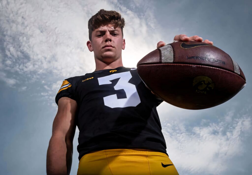 Cooper DeJean Iowa Hawkeyes football player holding ball confident against cloudy sky background Wallpaper