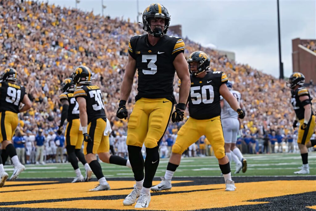 Cooper DeJean in black gold Iowa Hawkeyes uniform on football field with cheering crowd background Wallpaper