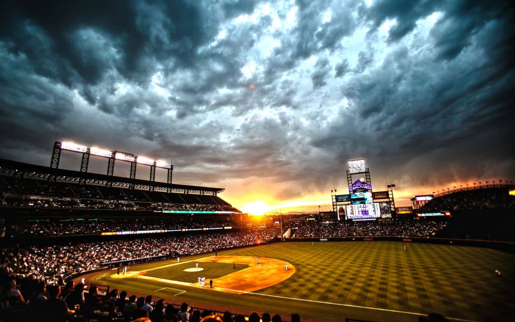 Coors Field baseball stadium at sunset with dramatic clouds glowing lights and cheering crowd Wallpaper