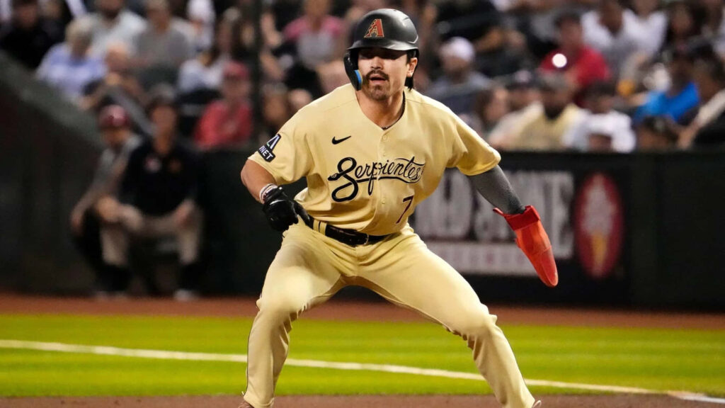 Corbin Carroll in cream Arizona Diamondbacks uniform poised to sprint on baseball field stadium background Wallpaper