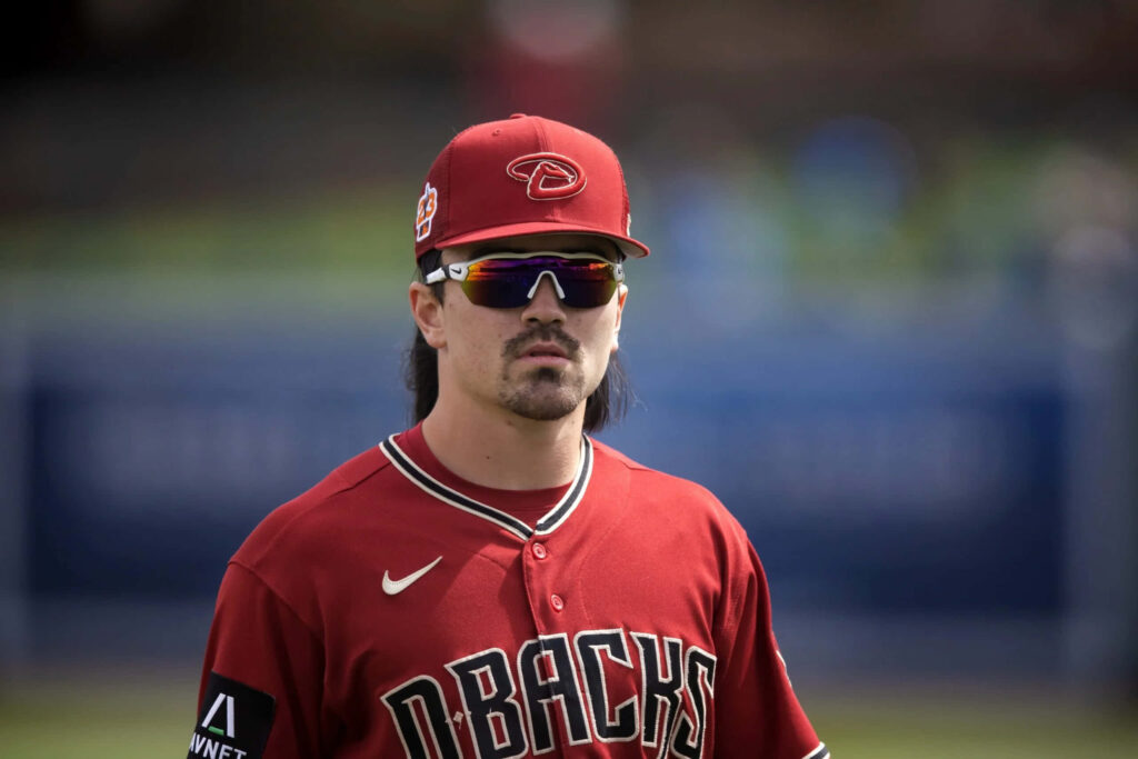 Corbin Carroll in red Arizona Diamondbacks uniform with sunglasses and cap on baseball field Wallpaper