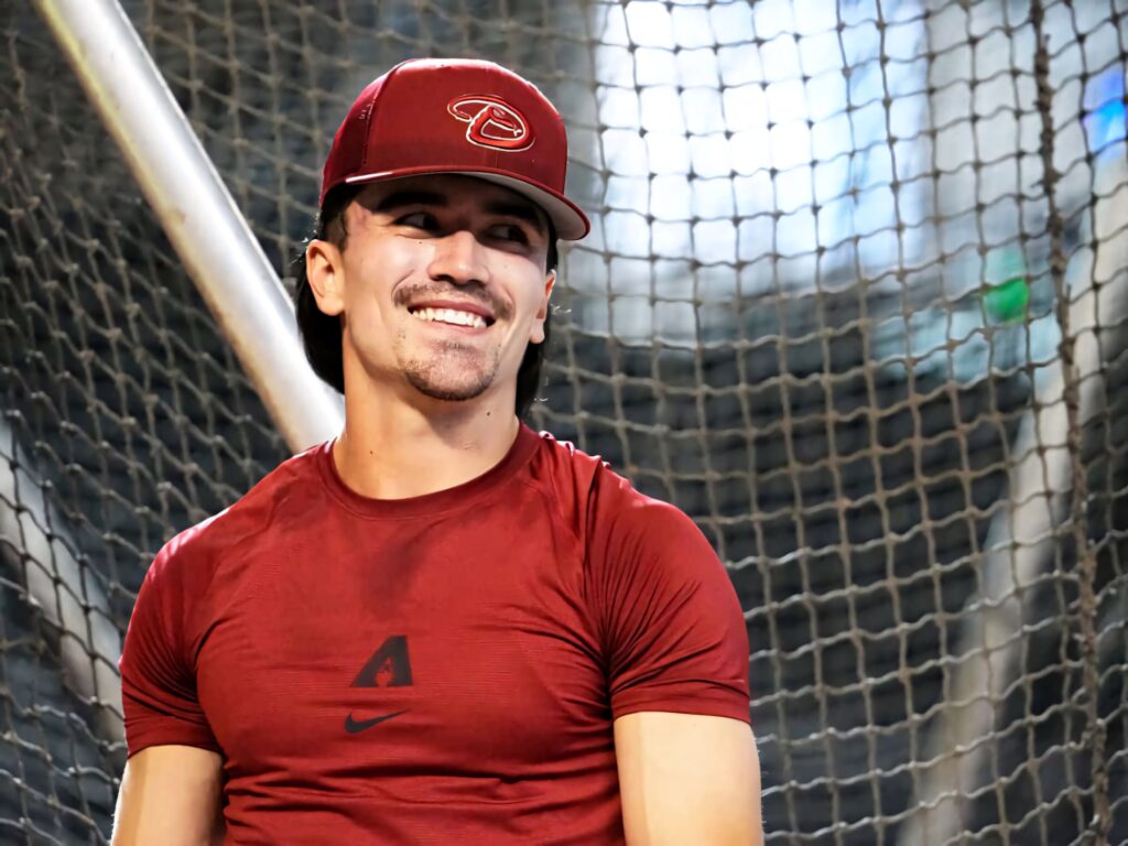 Corbin Carroll in red baseball uniform standing confidently with netted backdrop vibrant wallpaper