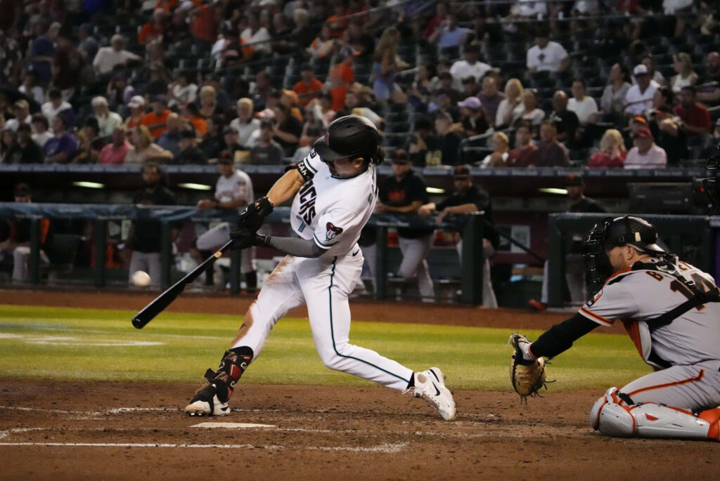Corbin Carroll swinging bat in Arizona Diamondbacks uniform under bright stadium lights Wallpaper