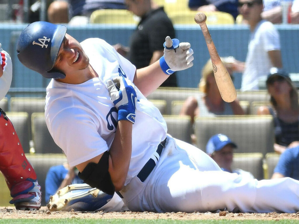 Corey Seager spinning bat midair smiling in Dodgers uniform at sunlit baseball stadium game Wallpaper