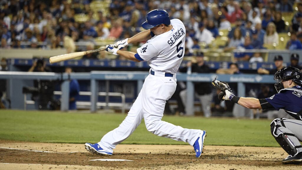 Corey Seager mid-swing in Los Angeles Dodgers uniform on vibrant baseball field with fans Wallpaper