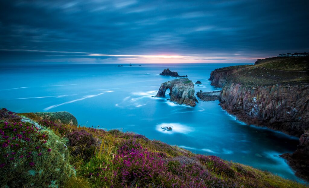 Rugged Cornwall cliffs and coastline with wildflowers under moody sky over calm Celtic Sea Wallpaper