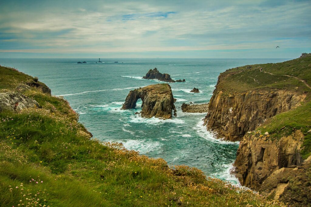 Dramatic Cornwall coastline with rugged cliffs lush grass ocean reefs natural arches and waves Wallpaper