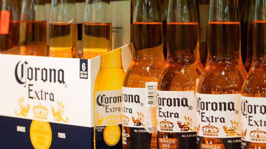 Close-up of Corona Extra beer bottles in six-pack carrier with golden lager glow wallpaper background
