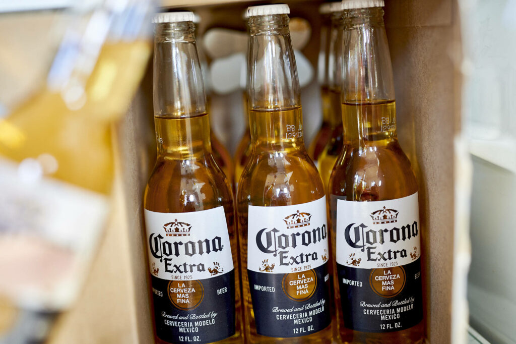 Close-up of Corona Extra beer bottles in cardboard box showcasing golden beer and labels Wallpaper