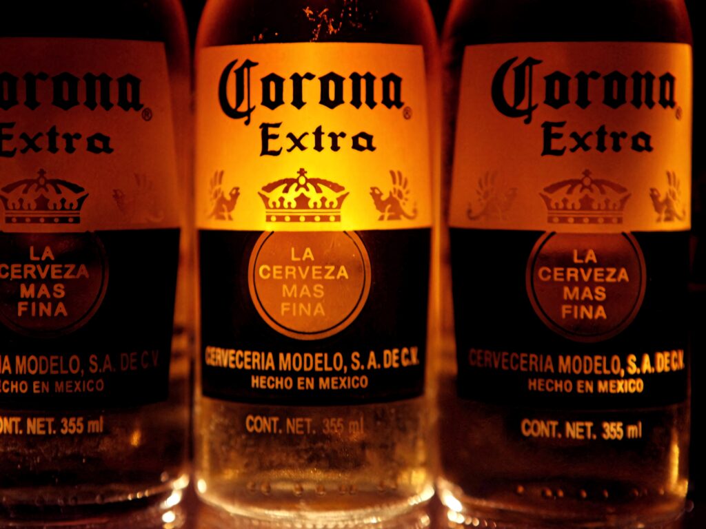 Close-up of Corona Extra beer bottles with golden amber lighting highlighting branded label wallpaper