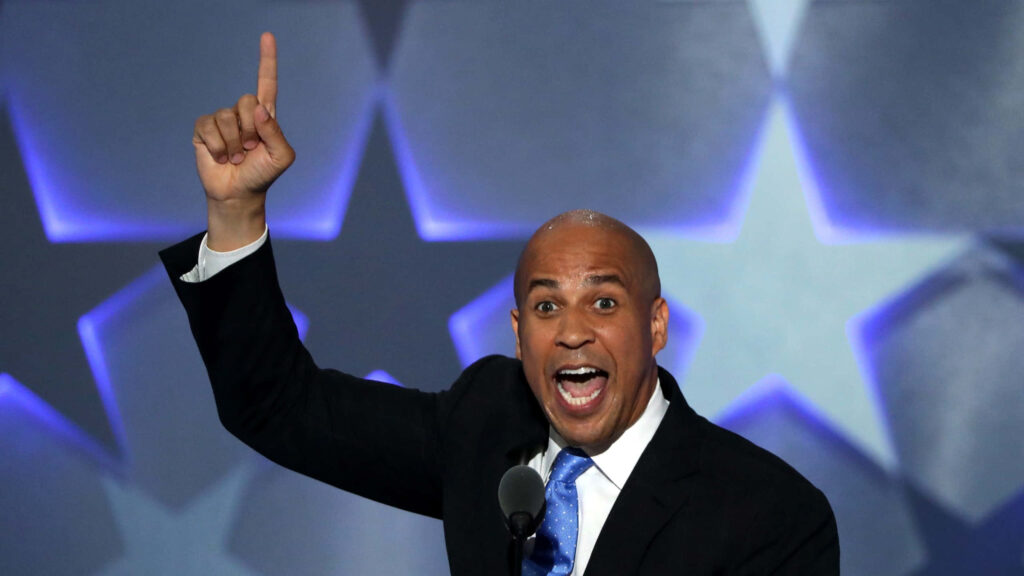 Cory Booker speaking energetically with vibrant blue purple stars background wallpaper