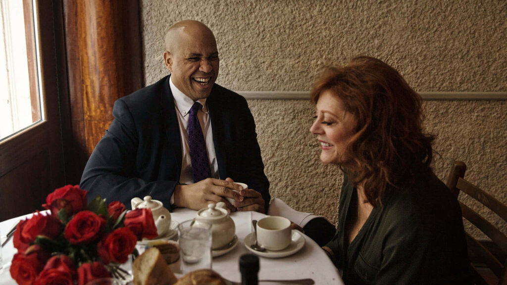 Cory Booker enjoying lively breakfast meeting with companion at warm restaurant table with red roses Wallpaper