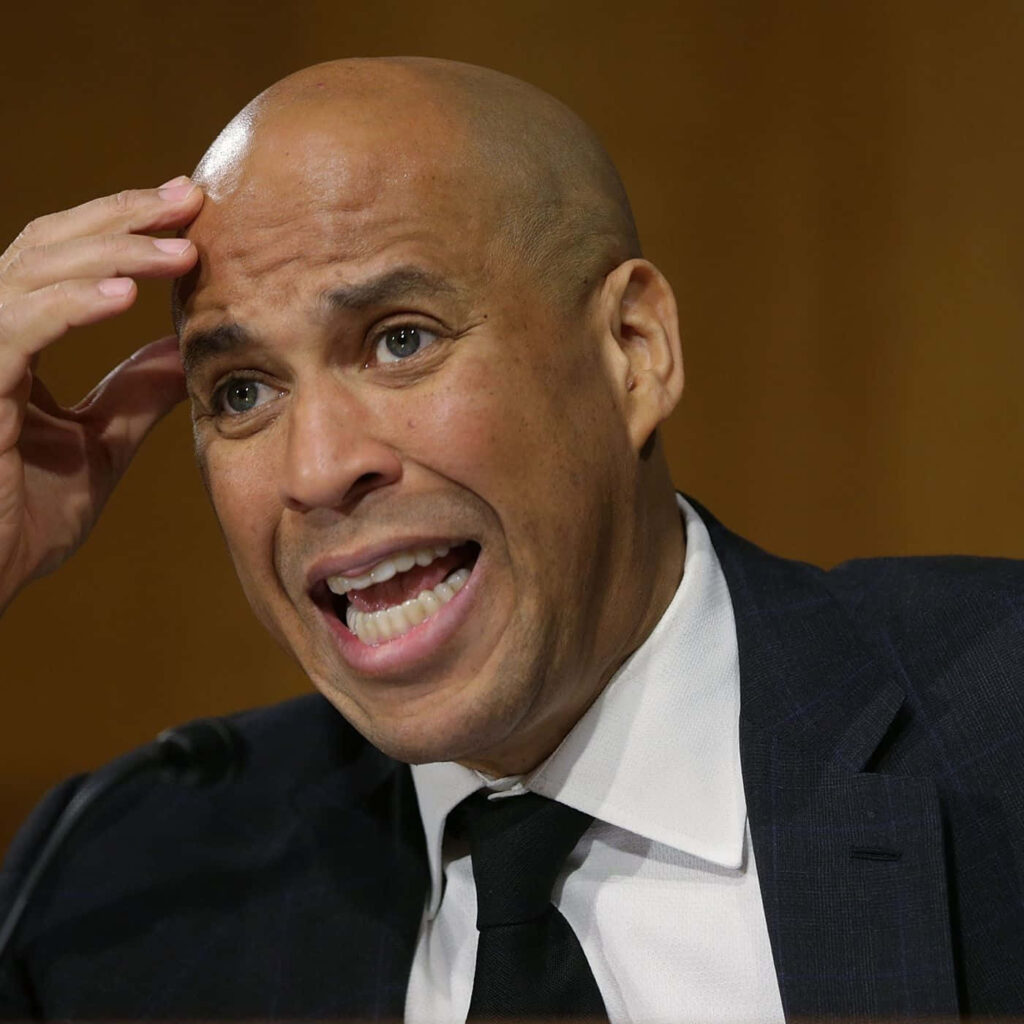 Cory Booker in dark suit showing frustration with expressive hand gesture indoor background Wallpaper