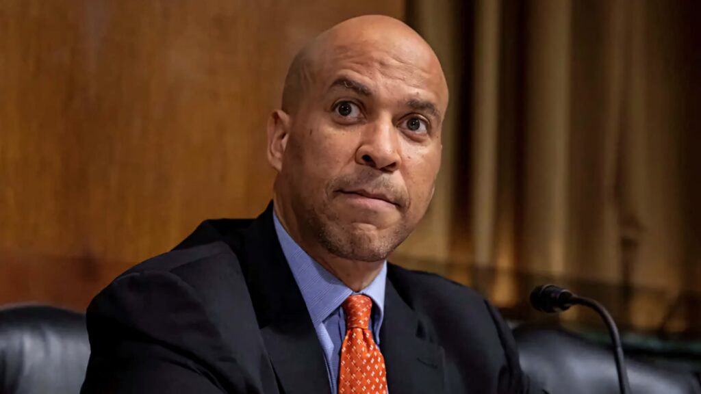 Cory Booker US senator in dark suit and orange tie with blurred background leadership wallpaper