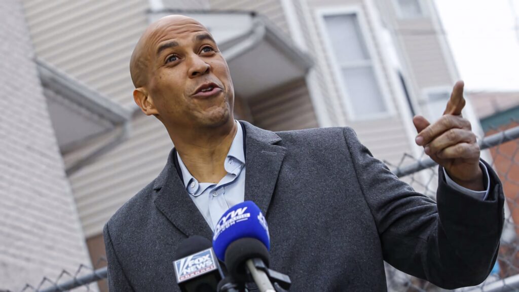 Cory Booker speaking to media outdoors with Fox News microphones in front of residential buildings Wallpaper