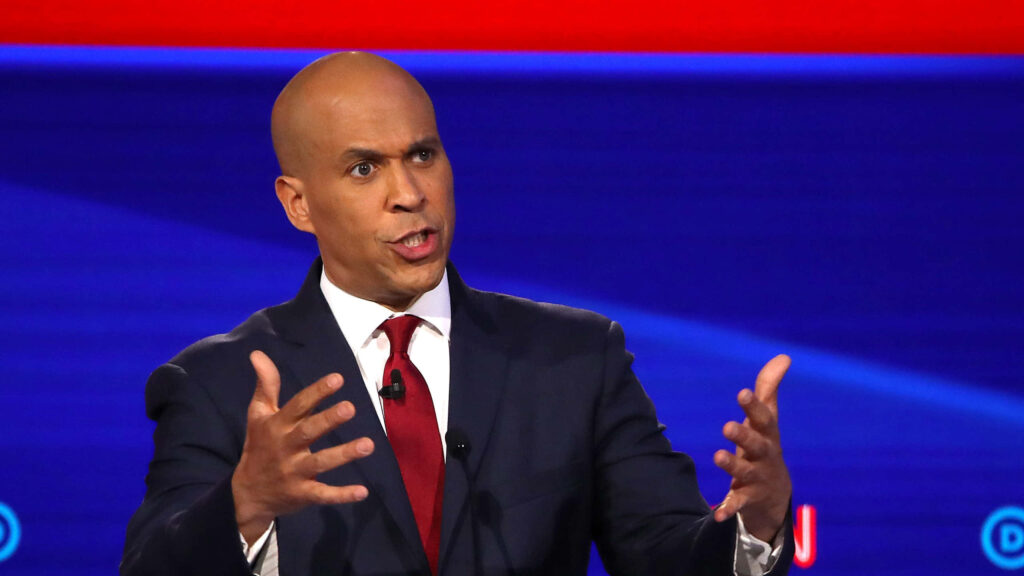 Cory Booker presidential campaign wallpaper showing him speaking on stage in navy suit and red tie