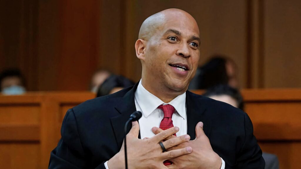Senator Cory Booker speaking at Senate hearing in suit and red tie with wood-paneled background Wallpaper