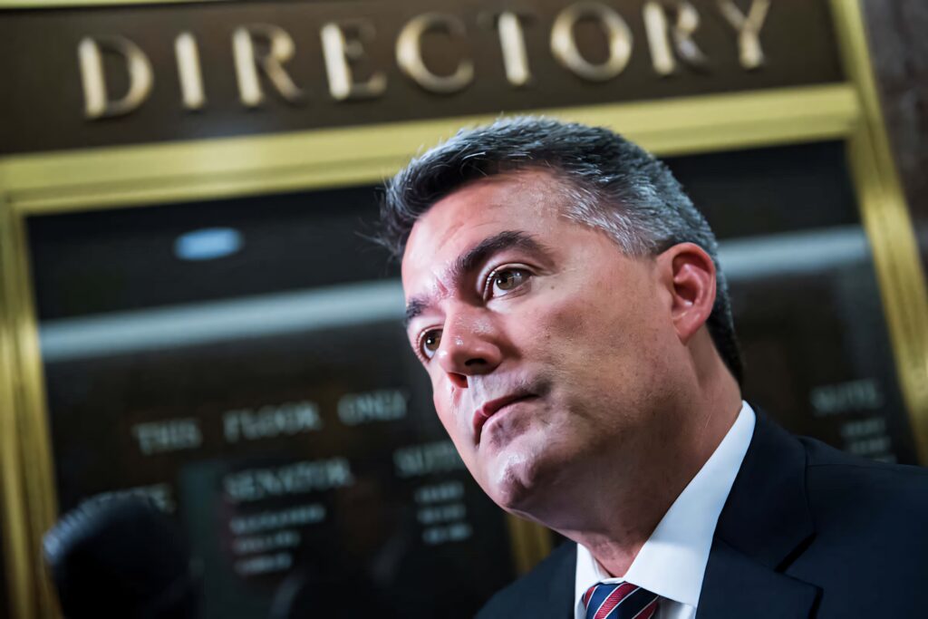Close-up of Cory Gardner in formal setting with directory sign and warm gold tones wallpaper