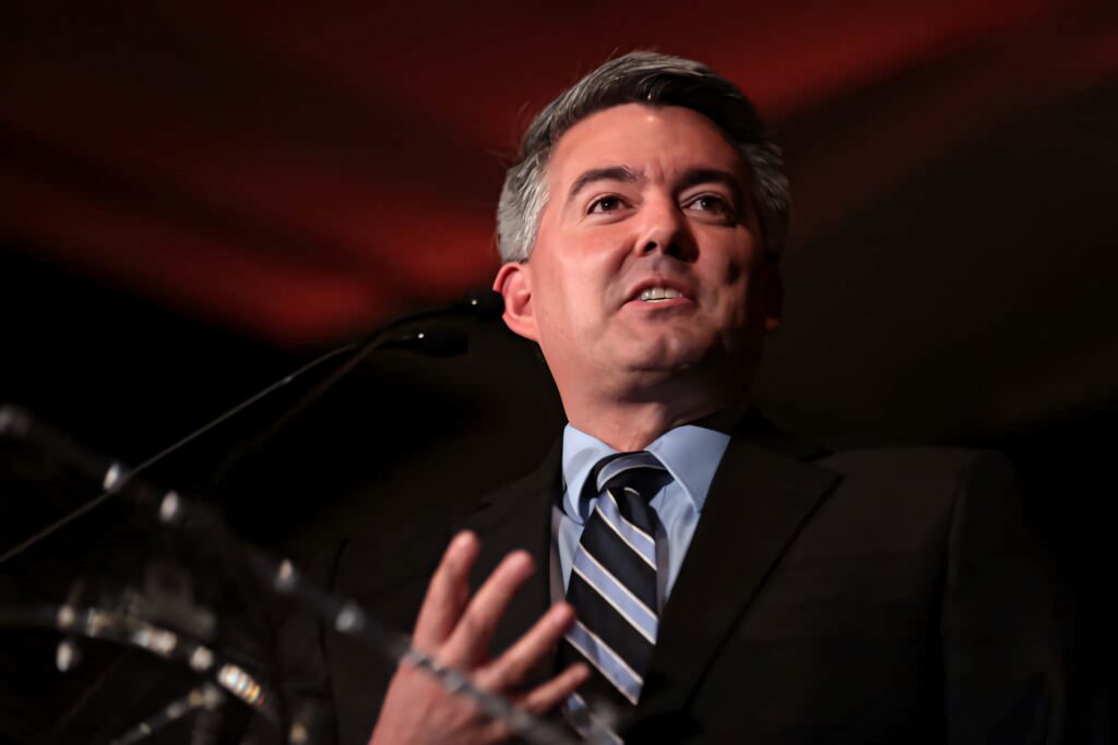 Cory Gardner in dark suit speaking at podium with red and black dramatic political background wallpaper
