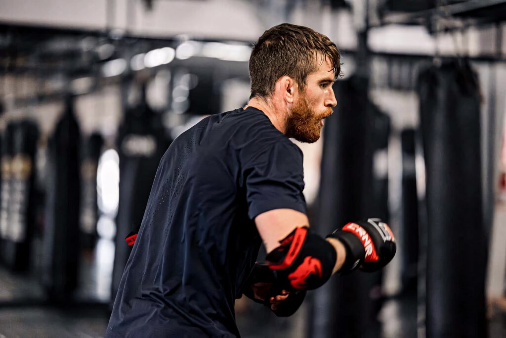 Cory Sandhagen focused in boxing gloves at gym training with punching bags and athletic gear Wallpaper