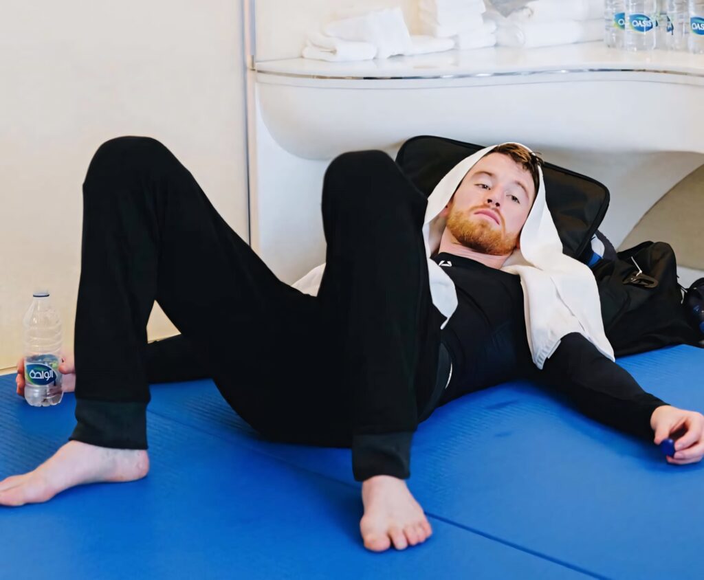 Cory Sandhagen resting on blue gym mat with towel and water bottle in modern training gym Wallpaper