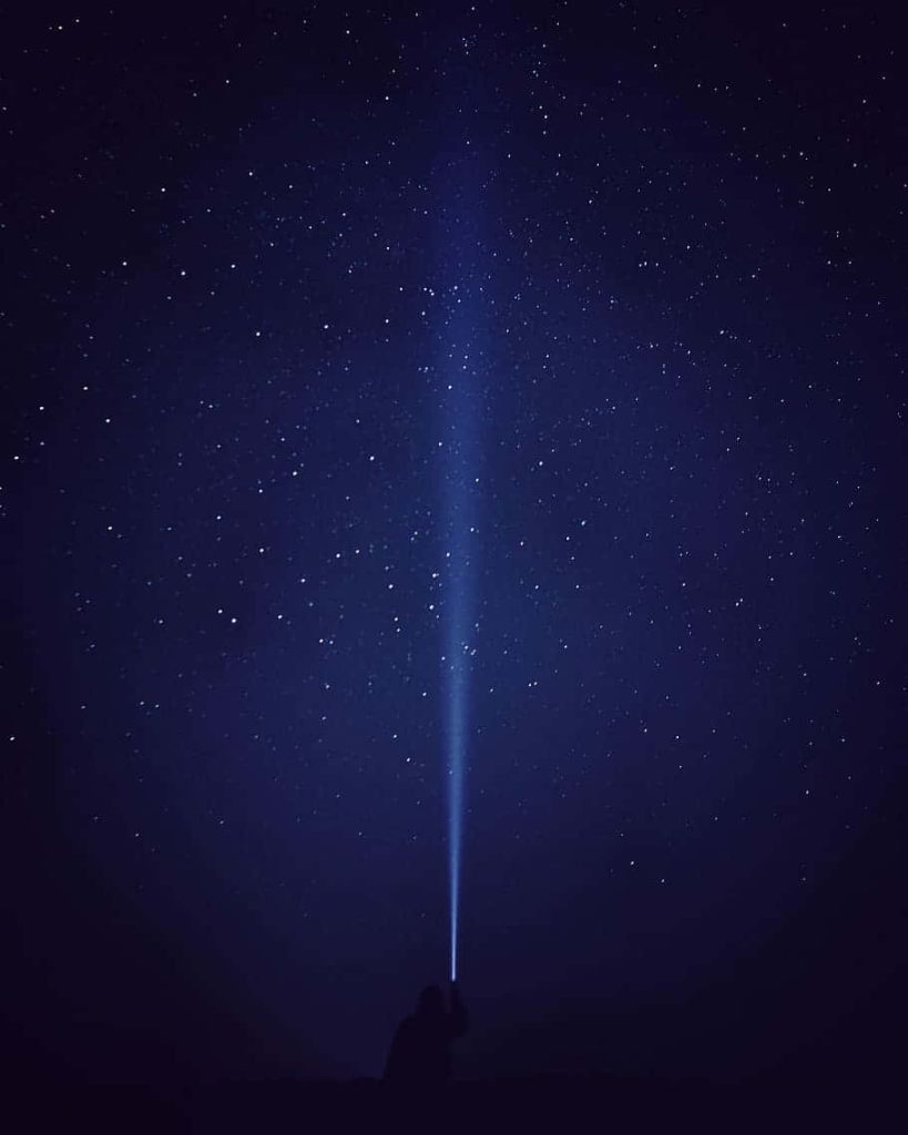 Silhouette with flashlight beam under vast starry night sky deep blue minimalist wallpaper background