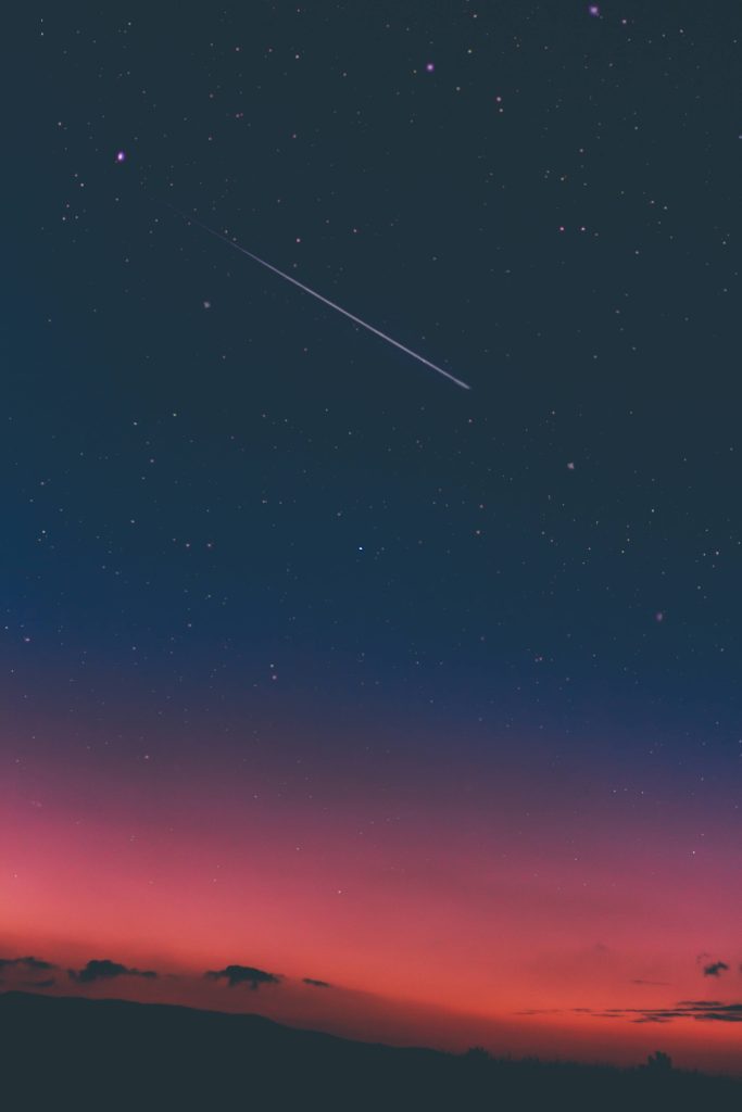 Vertical wallpaper of vibrant twilight sky and shooting star over silhouetted hills perfect background