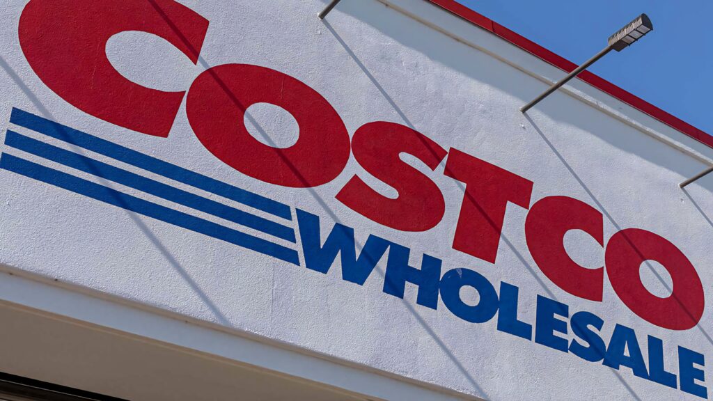 Close-up of Costco Wholesale sign with bold red and blue text on bright white background Wallpaper