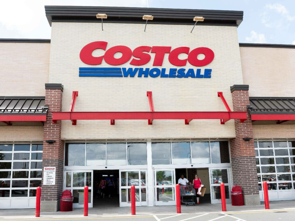 Costco Wholesale store entrance with red blue logo beige brick facade and busy customers walking Wallpaper