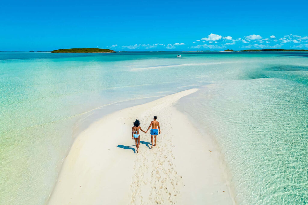 Couple Strolling Hand-in-Hand on a Tranquil Beach with Turquoise Waters Wallpaper