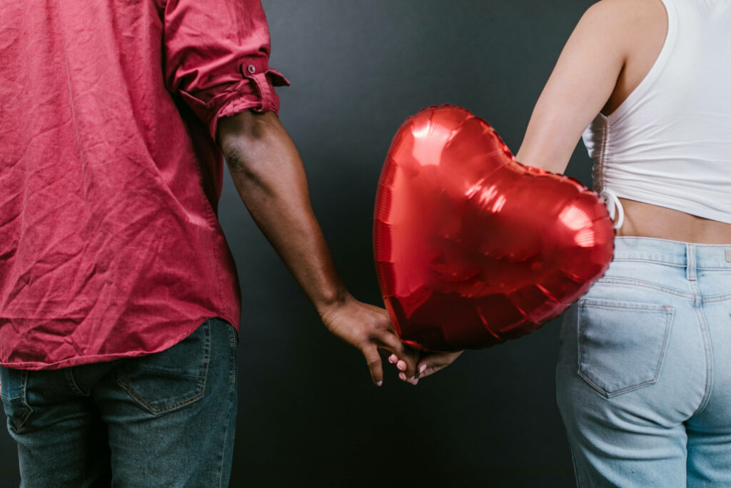 Love's Tender Embrace: Intertwined Hands Grasping a Vibrant Heart Balloon Wallpaper