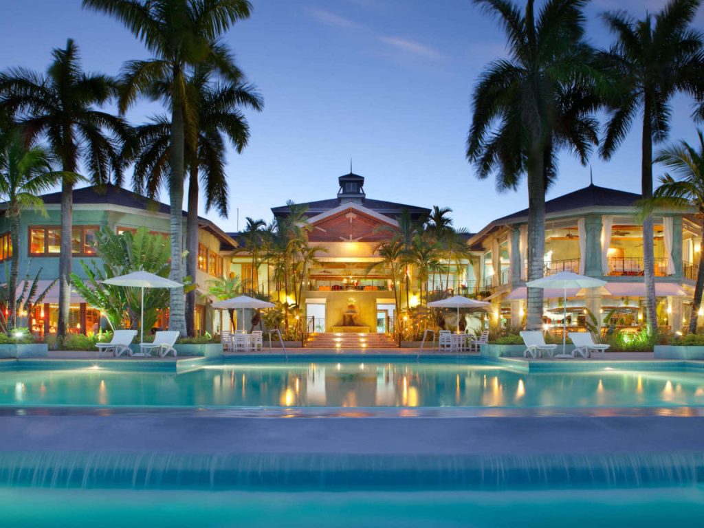 Twilight view of Couples Sans Souci Jamaica infinity pool with palm trees and warm hotel lights Wallpaper