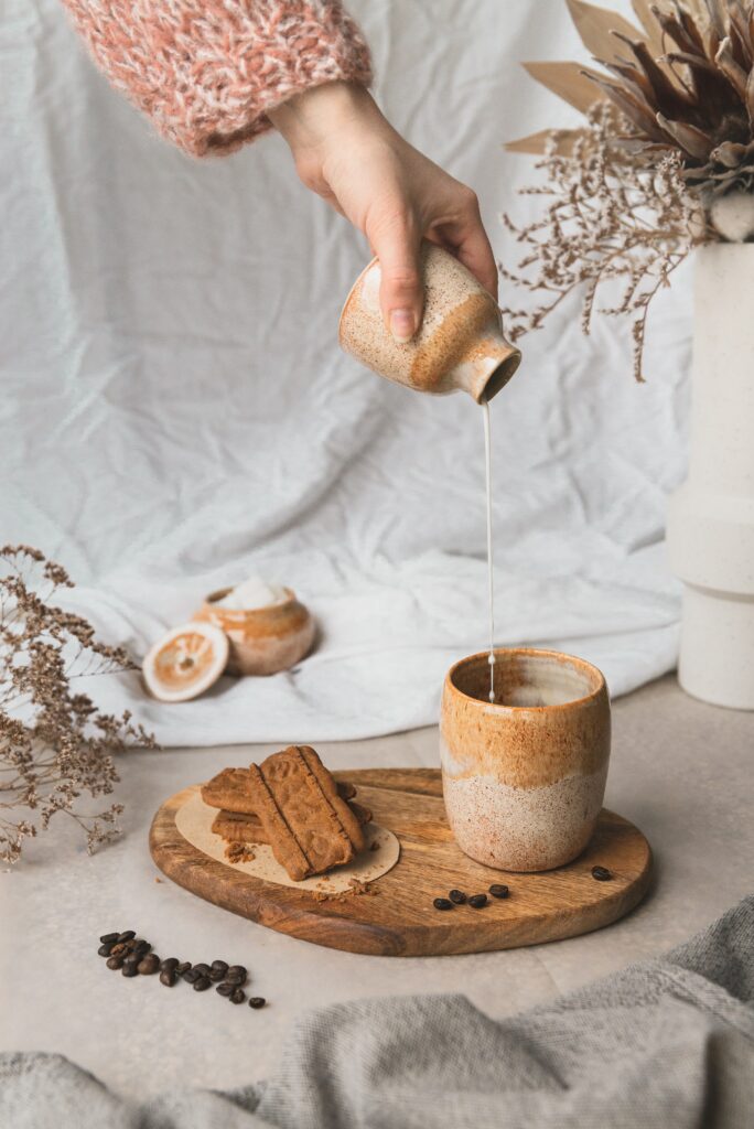 Cozy Aesthetic Setup: Hand Pouring Milk into Rustic Cup with Cookies Wallpaper