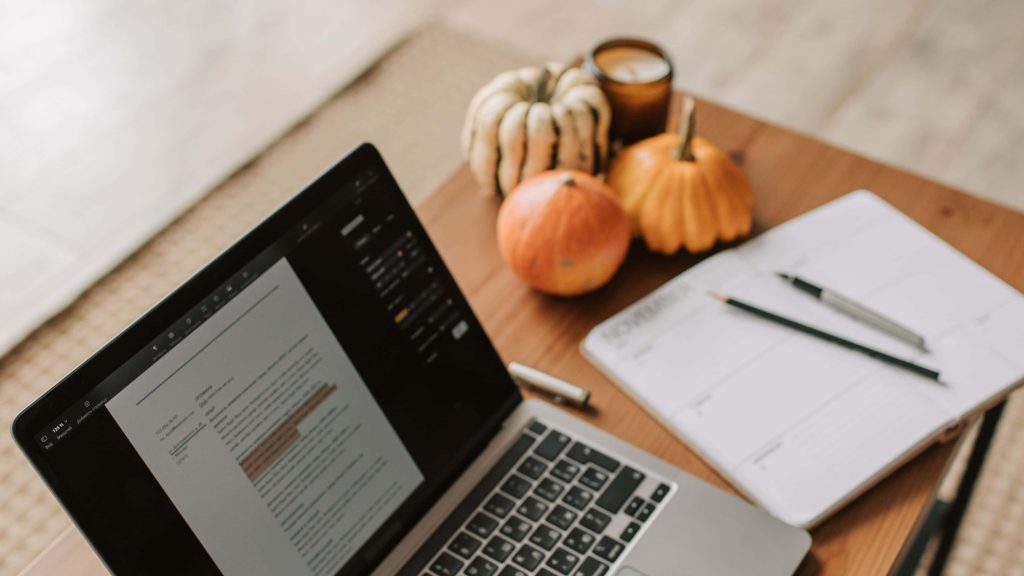 Cozy autumn workspace with laptop planner candle pumpkins warm natural light wooden desk Wallpaper