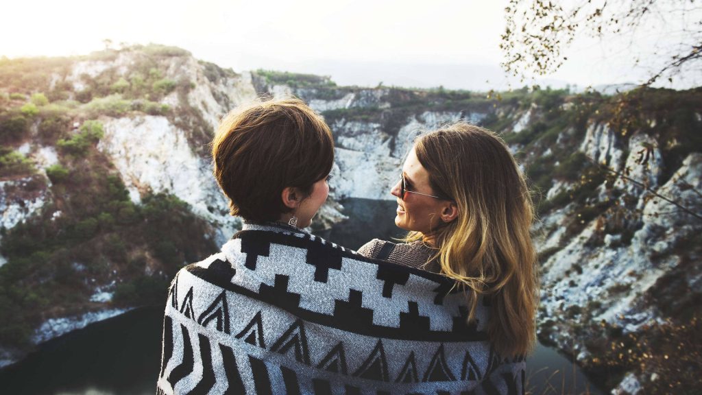 Two friends wrapped in a black and white geometric blanket overlooking rocky quarry at sunset Wallpaper
